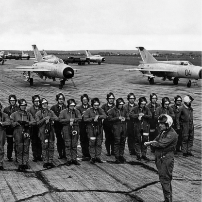 Group of people in uniform standing on an airfield with aircraft in the background, on Soviet hexagon tarmac